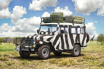 A safari-style off-road vehicle with a bold black and white zebra stripe pattern, parked in a grassy savanna landscape under a blue sky with clouds. Zebras and a giraffe are visible in the background.