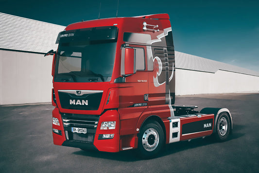 Red MAN truck on a road with a white building in the background