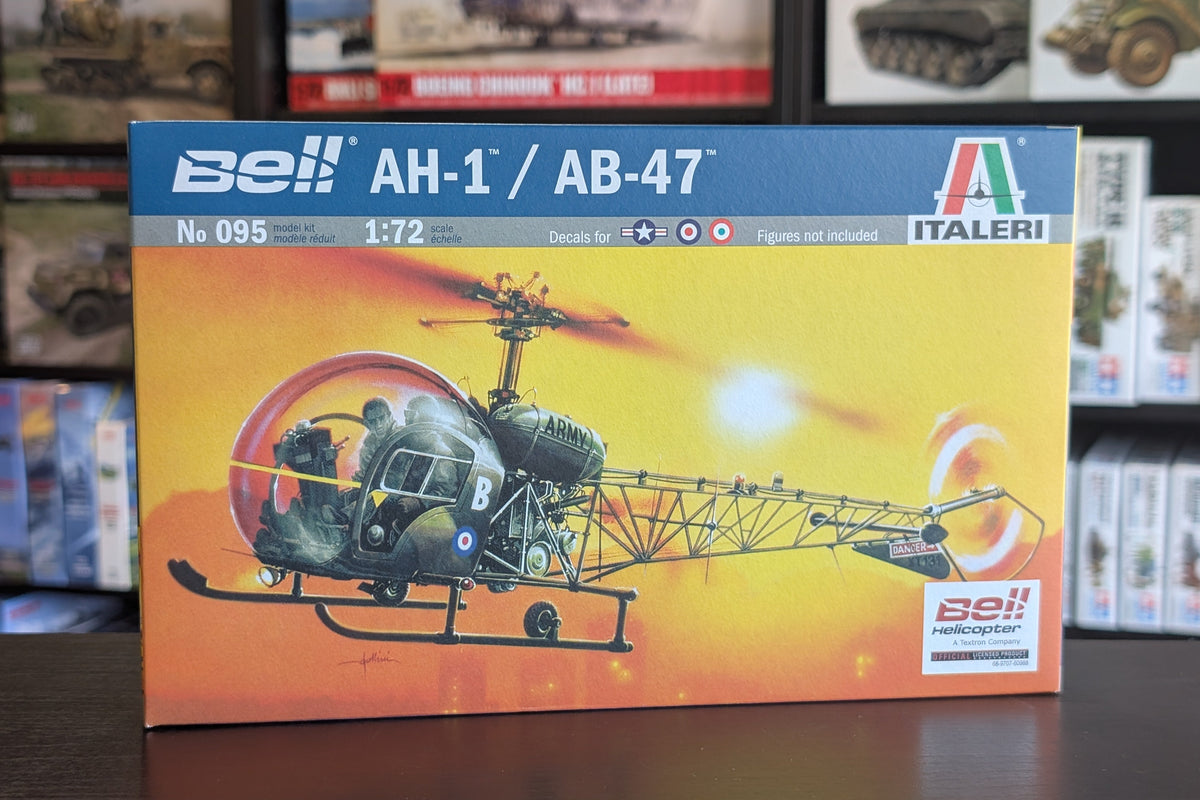 A boxed model kit for Bell AH-1 and AB-47 helicopters, shown standing on a dark tabletop with shelves of other boxes in the background. The front of the box features a blue header with the Bell and Italeri branding and a large illustration of the helicopters in green, black, and orange tones.