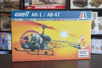 A boxed model kit for Bell AH-1 and AB-47 helicopters, shown standing on a dark tabletop with shelves of other boxes in the background. The front of the box features a blue header with the Bell and Italeri branding and a large illustration of the helicopters in green, black, and orange tones.