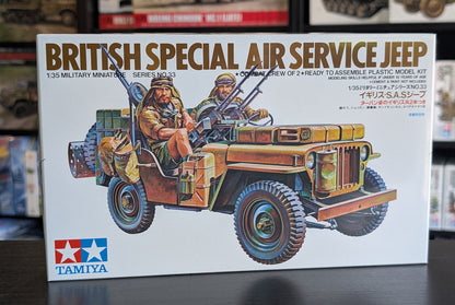 Tamiya British Special Air Service Jeep model kit box, featuring an illustration of the assembled military miniature vehicle with two crew members, photographed on a dark tabletop with blurred model kit boxes in the background.